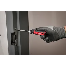 A gloved hand uses the #2 Phillips 4" Cushion Grip Screwdriver (USA) to tighten screws on a door lock mechanism. The screwdriver is red and black with a comfortable grip, ensuring ease of use during tasks.