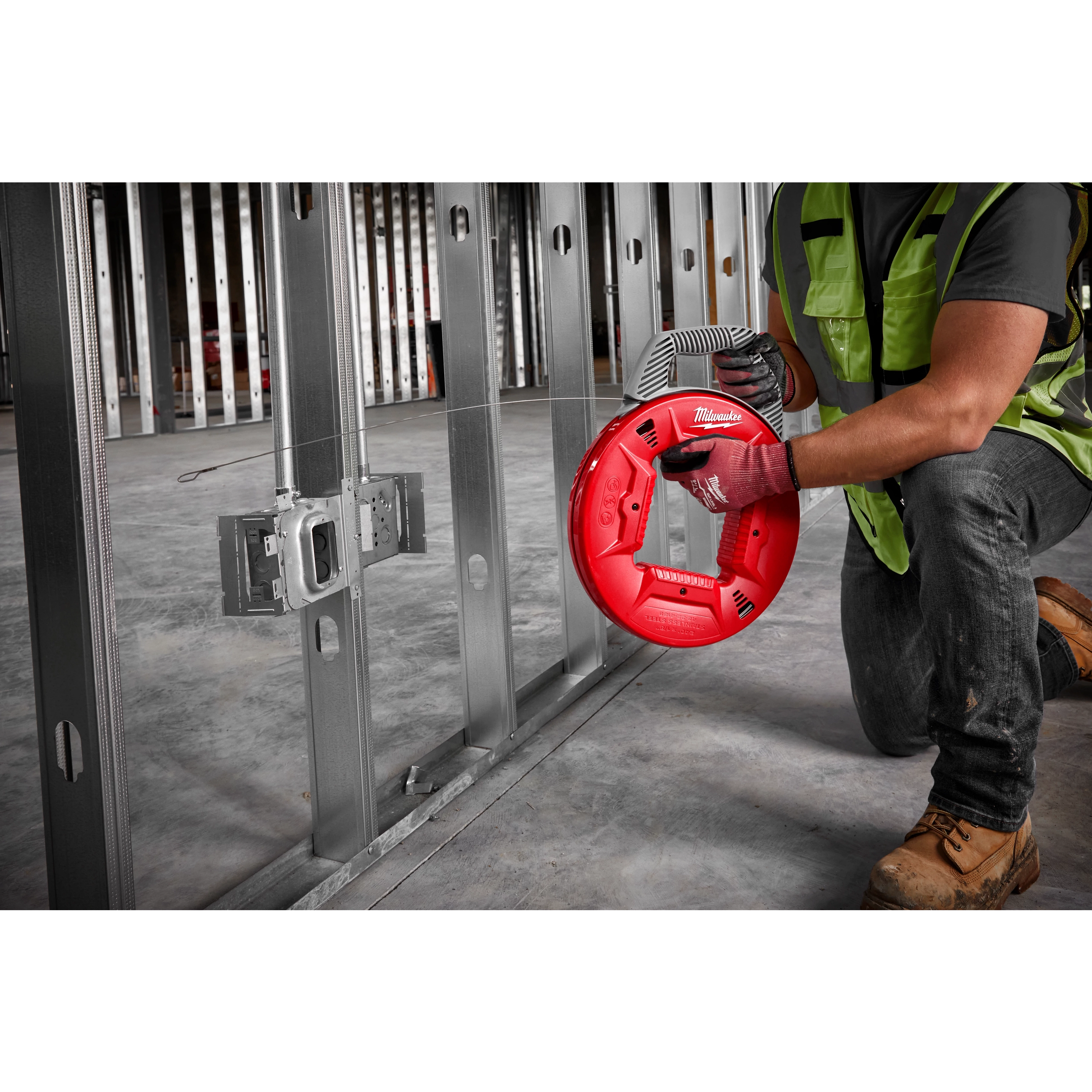 A construction worker using a 240' 1/8" Stainless Steel Fish Tape to guide wiring through metal studs in an unfinished wall.