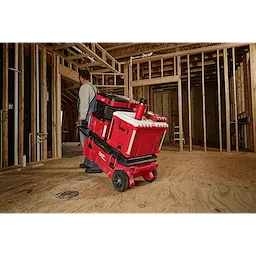 Man pulling a stack of red tool storage boxes on a cart in a construction site, with a PACKOUT 18oz Insulated Mug with Sip Lid on top.