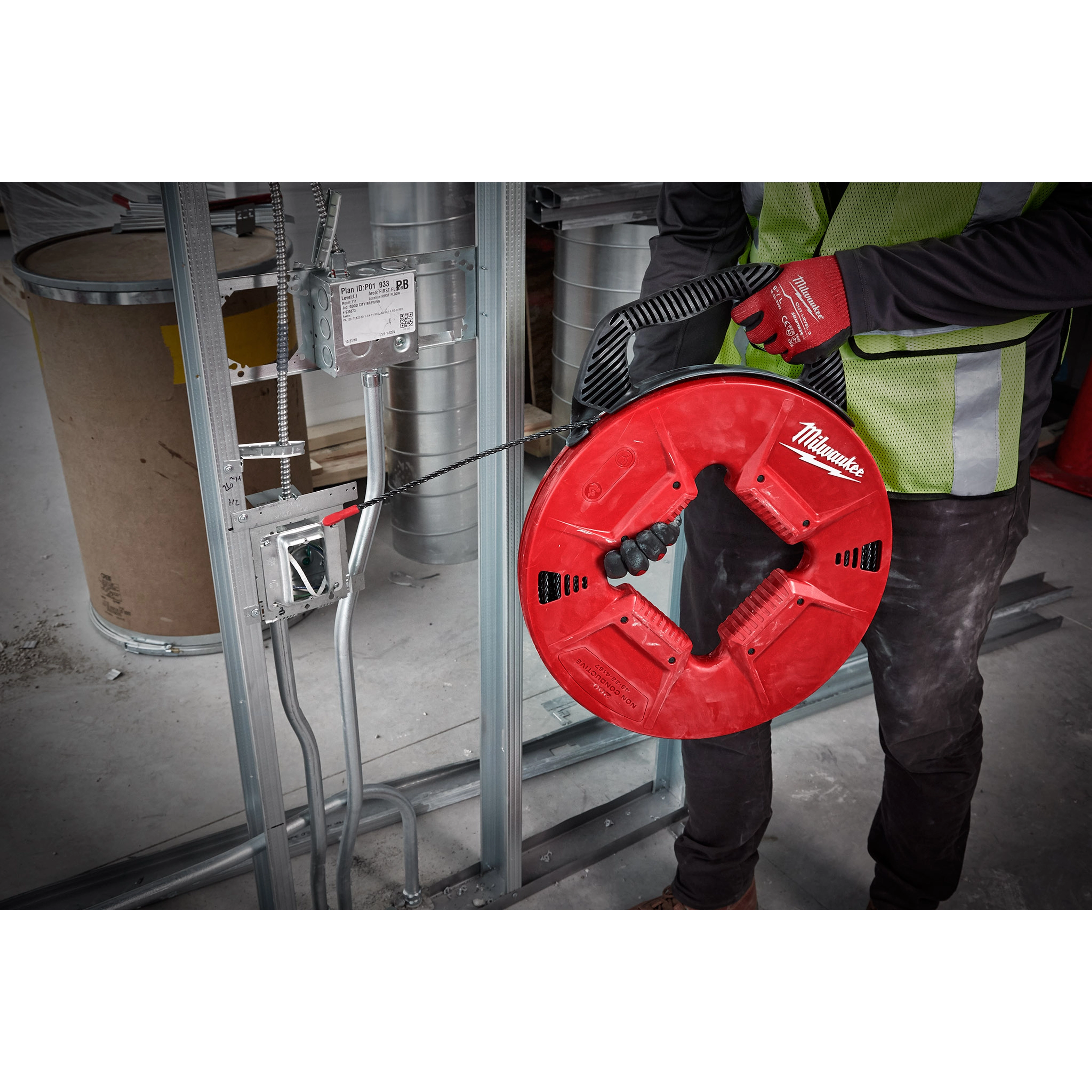 Person using 200% Polyester Fish Tape with Non-conductive Tip to pull wires through metal framing at a construction site.