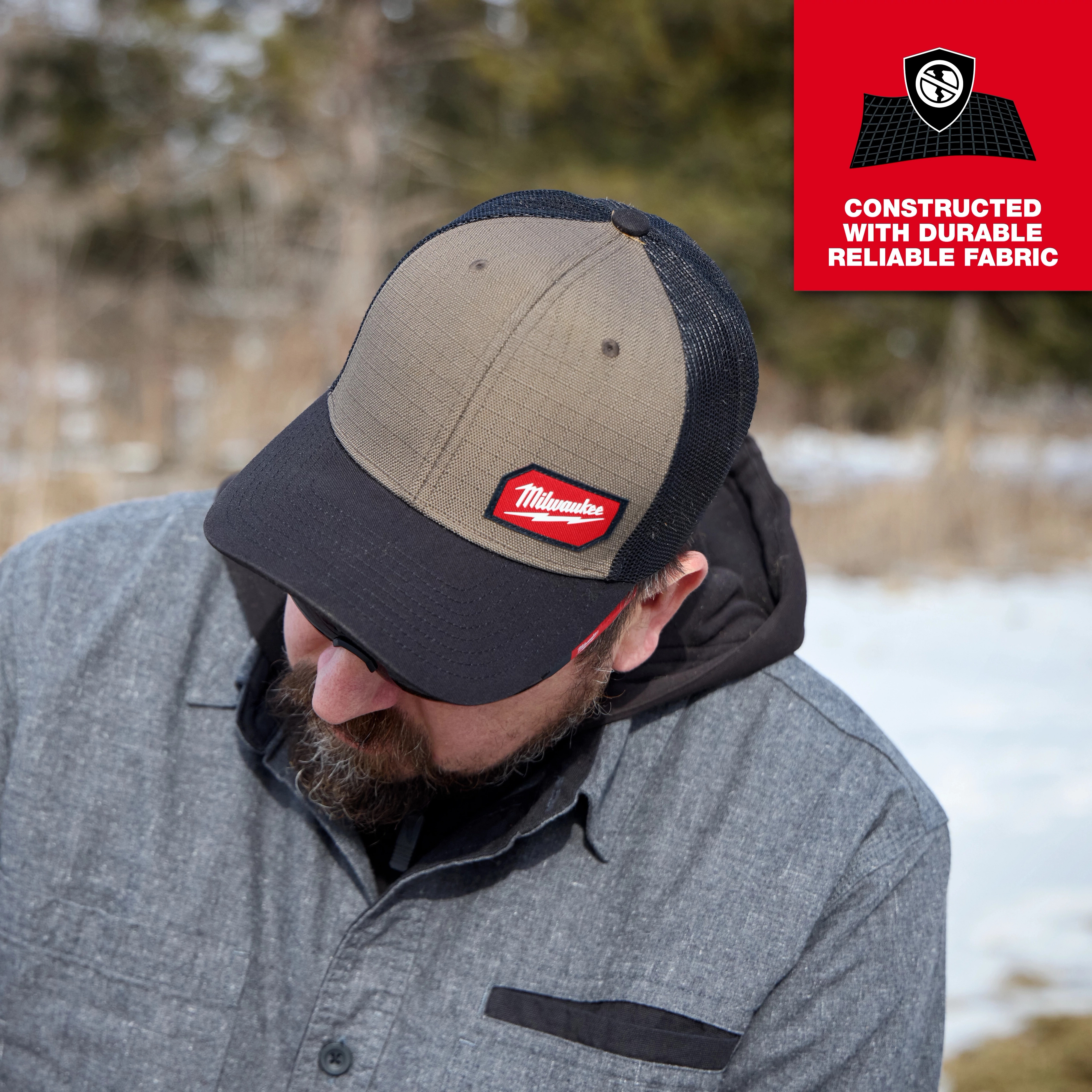 Person outdoors wearing a GRIDIRON Snapback Trucker Hat with a fabric durability message in the corner.