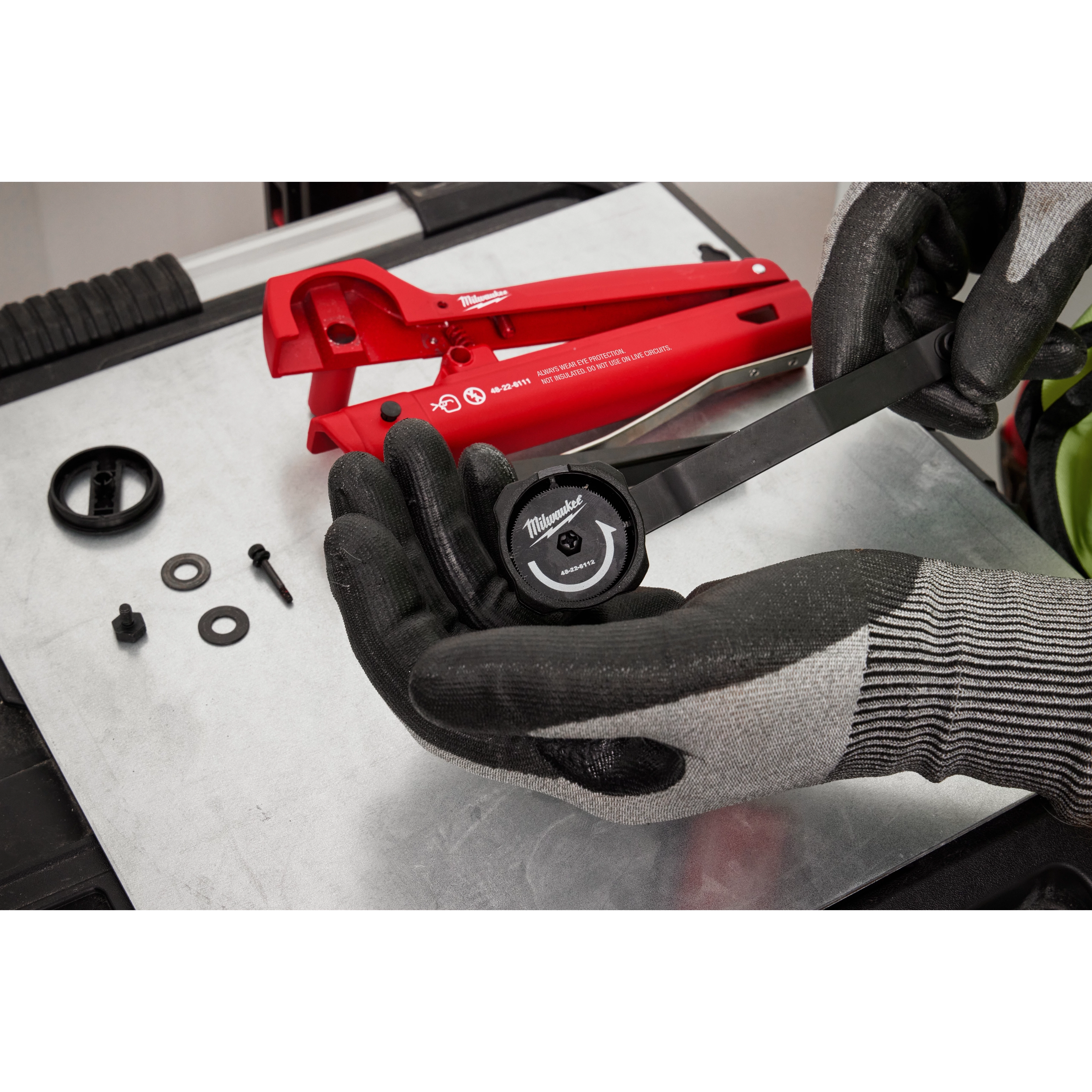 Armored Cable Cutter on a workbench with gloves, washers, bolts, and adjustment dial. The cutter is red and labeled with usage instructions.