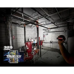 Person using a flashlight in a dimly lit industrial setting, illuminating pipes and machinery. Overlay text: "App%20Shot%20with%20overlay," "325 lumens," "TRUEVIEW High Definition Output."