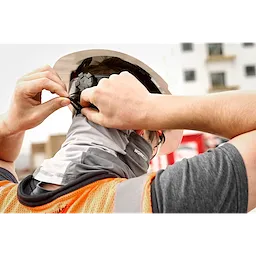 Person wearing a hard hat adjusting the WORKSKIN Performance Neck Gaiter at a construction site, also wearing an orange safety vest.