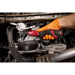 A person wearing an orange glove uses the M12 FUEL 1/4" Extended Reach Ratchet to work on engine components. The ratchet's compact design allows access to tight spaces, and its handle provides a secure grip.