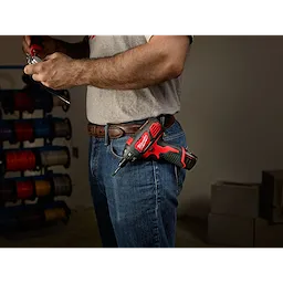 The M12 Screwdriver is clipped to a person's belt as they work with a tool in hand. The screwdriver is red and black.