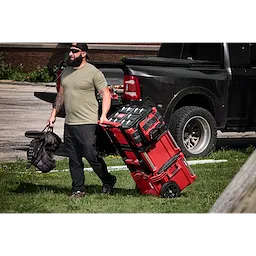 Worker pulling stacked tool boxes featuring the M18 TOP-OFF 350W Power Supply & Charger w/ PACKOUT Compatibility.