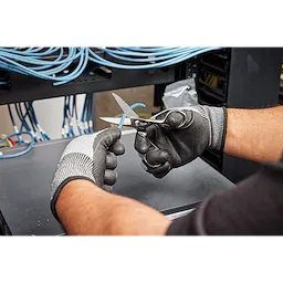 A person wearing gloves uses Electrician Scissors to cut a blue wire in a server room with blue cables in the background.