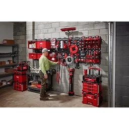 Man organizing tools in a garage using March 2023 Packout Shop Storage system with red toolboxes and wall-mounted storage units.