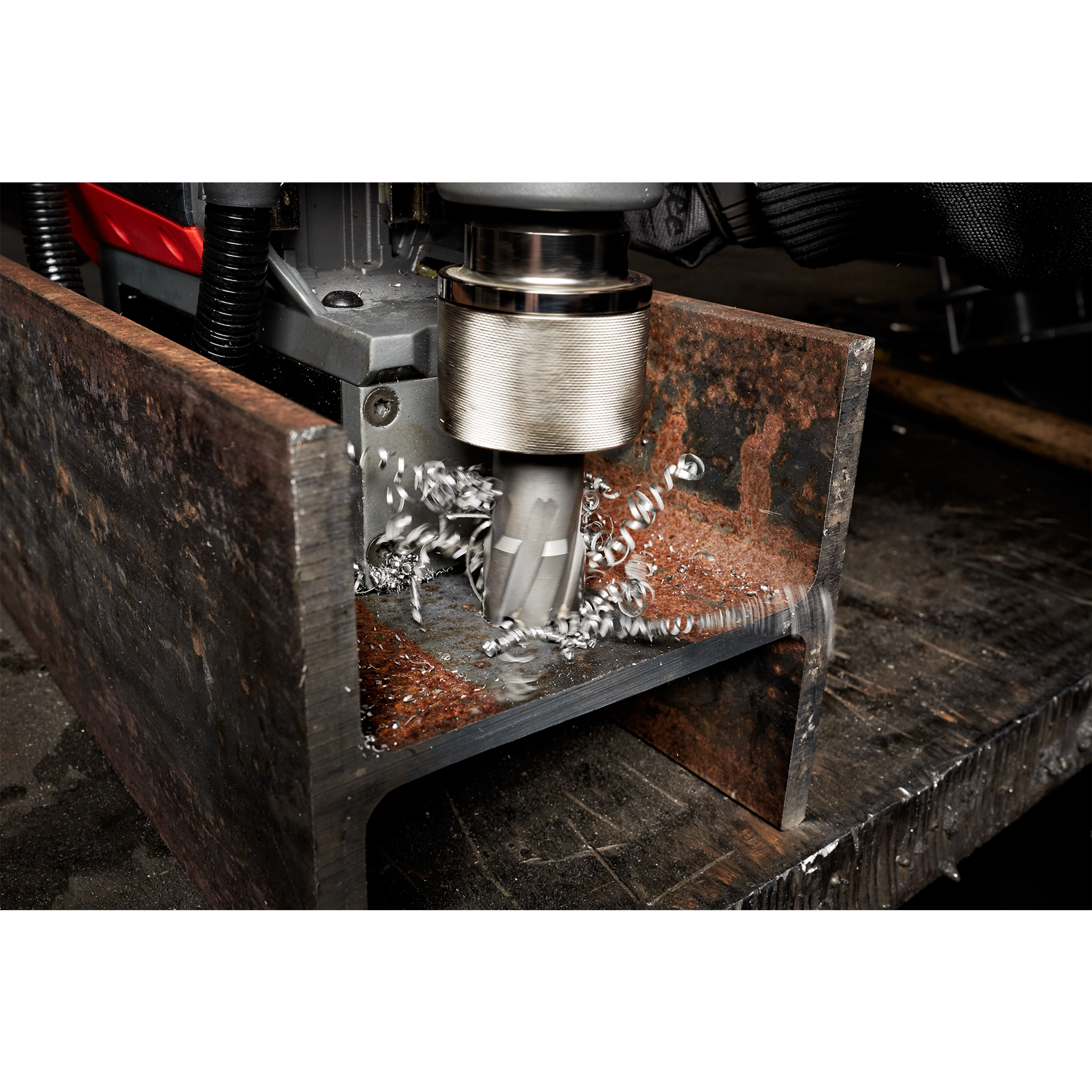 Annular Cutter drilling through a rusted metal piece, creating spiral metal shavings. The tool is held in a drilling machine.