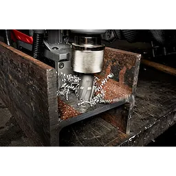 Annular Cutter drilling through a rusted metal piece, creating spiral metal shavings. The tool is held in a drilling machine.
