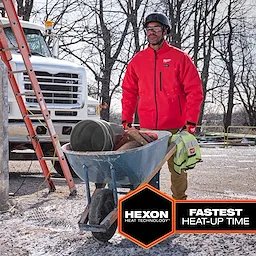 Worker wearing a red M12 Heated TOUGHSHELL Jacket while carrying a wheelbarrow filled with tools on a construction site.
