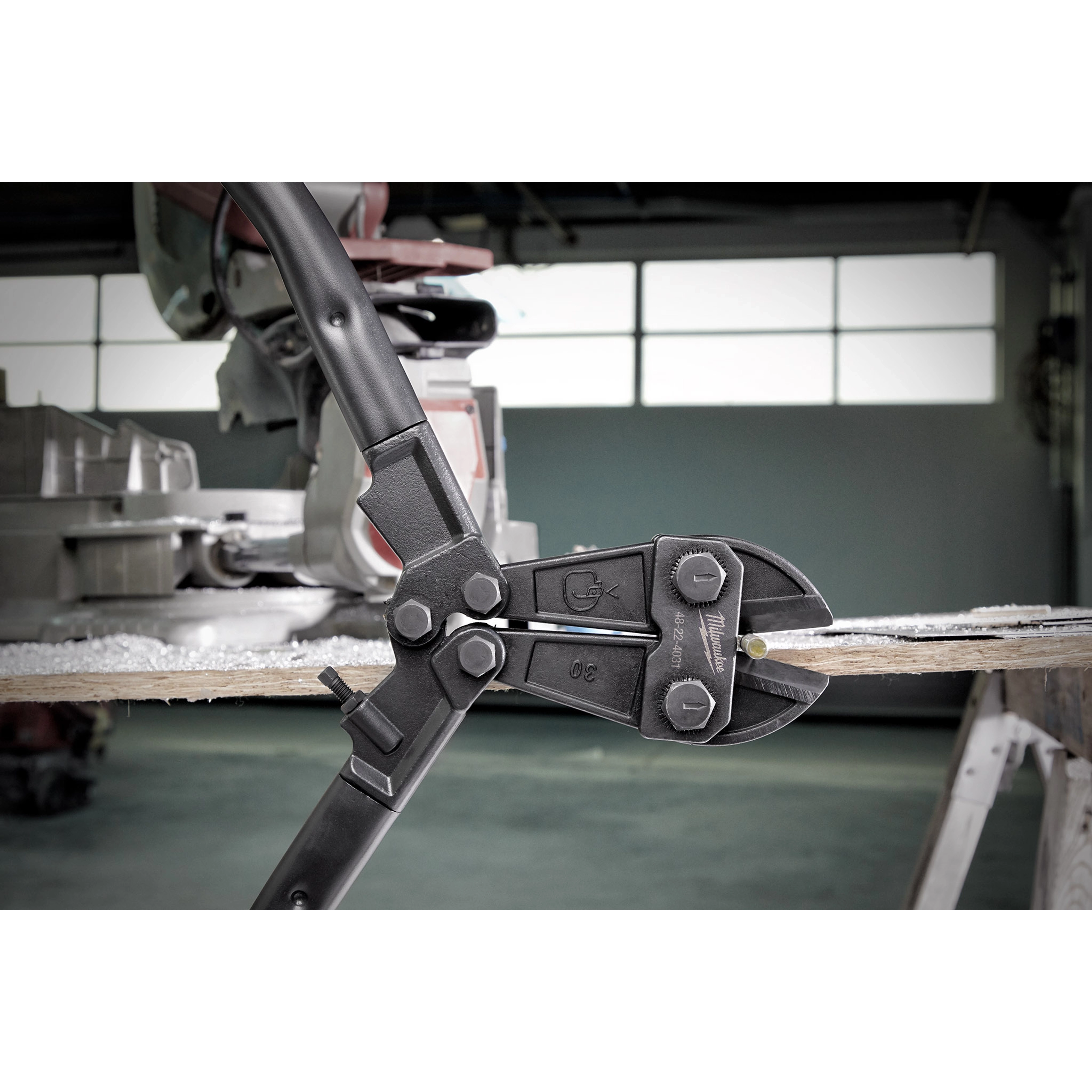 30" Bolt Cutter with black handles and jaws cutting through a piece of wood in a workshop with a window in the background.