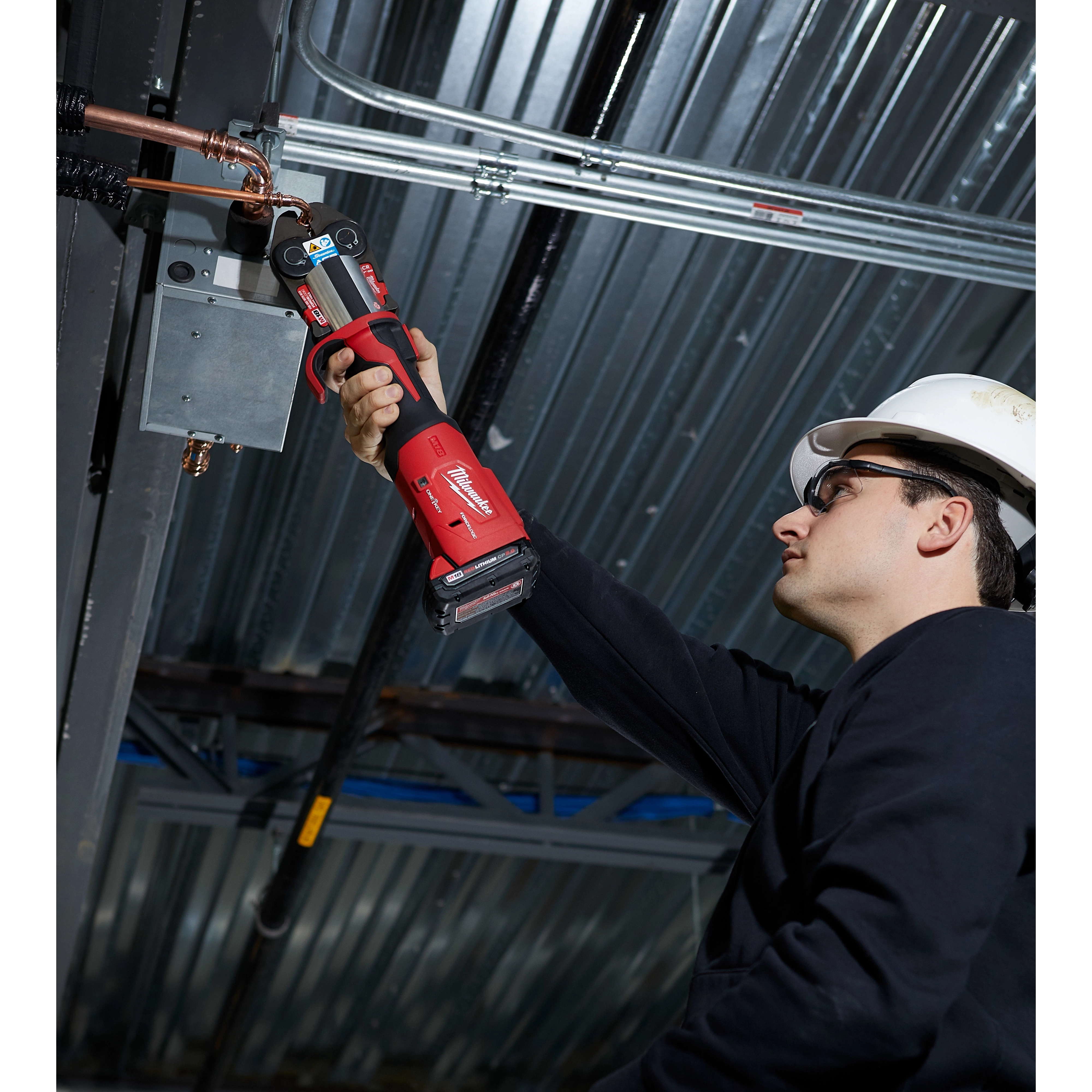 A person uses the M18 FORCE LOGIC Press Tool Kit with One-Key and 1/4"-7/8" Streamline ACR Jaws to fix a pipe overhead.