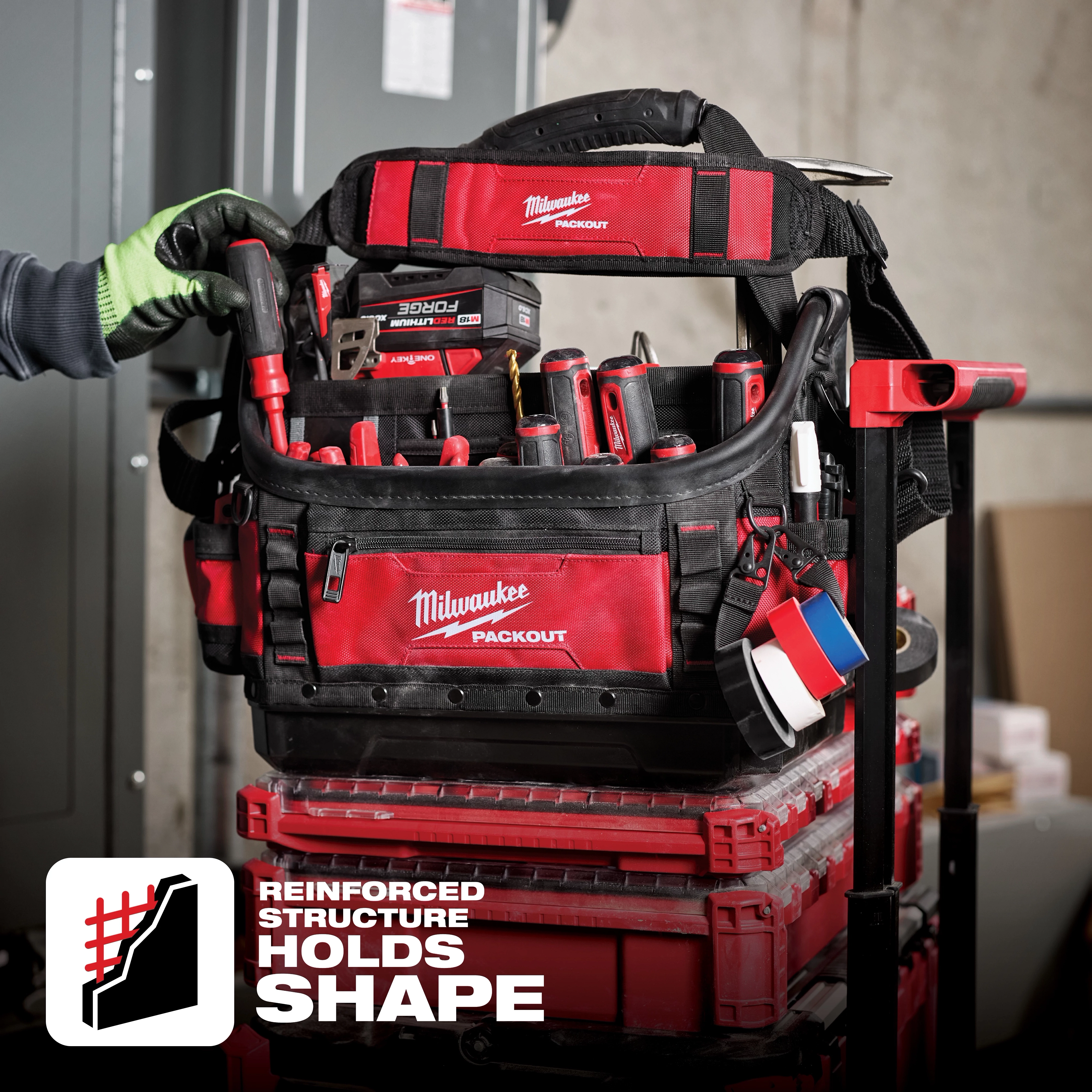 App%20Shot%20Overlay: A Milwaukee Packout tool bag filled with various tools, placed atop a stack of red toolboxes. Text states "Reinforced Structure Holds Shape."