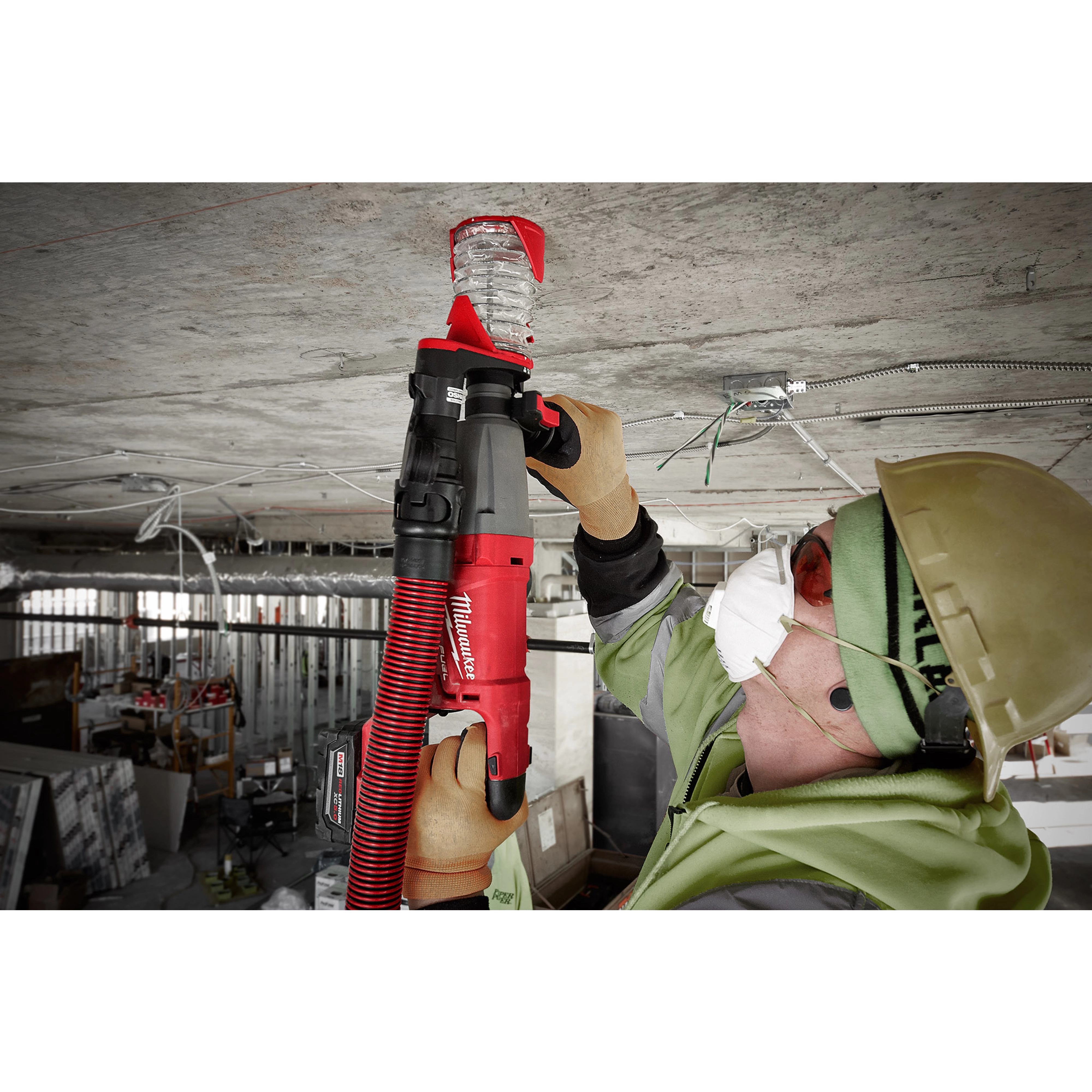 Worker using SDS+ DUST TRAP Drilling Shroud Bulk 10 to drill into a concrete ceiling, wearing safety gear and a dust mask.