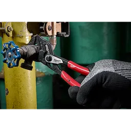 A gloved hand is using a 7" Pliers Wrench with black and red handles to turn a valve attached to a yellow pipe.