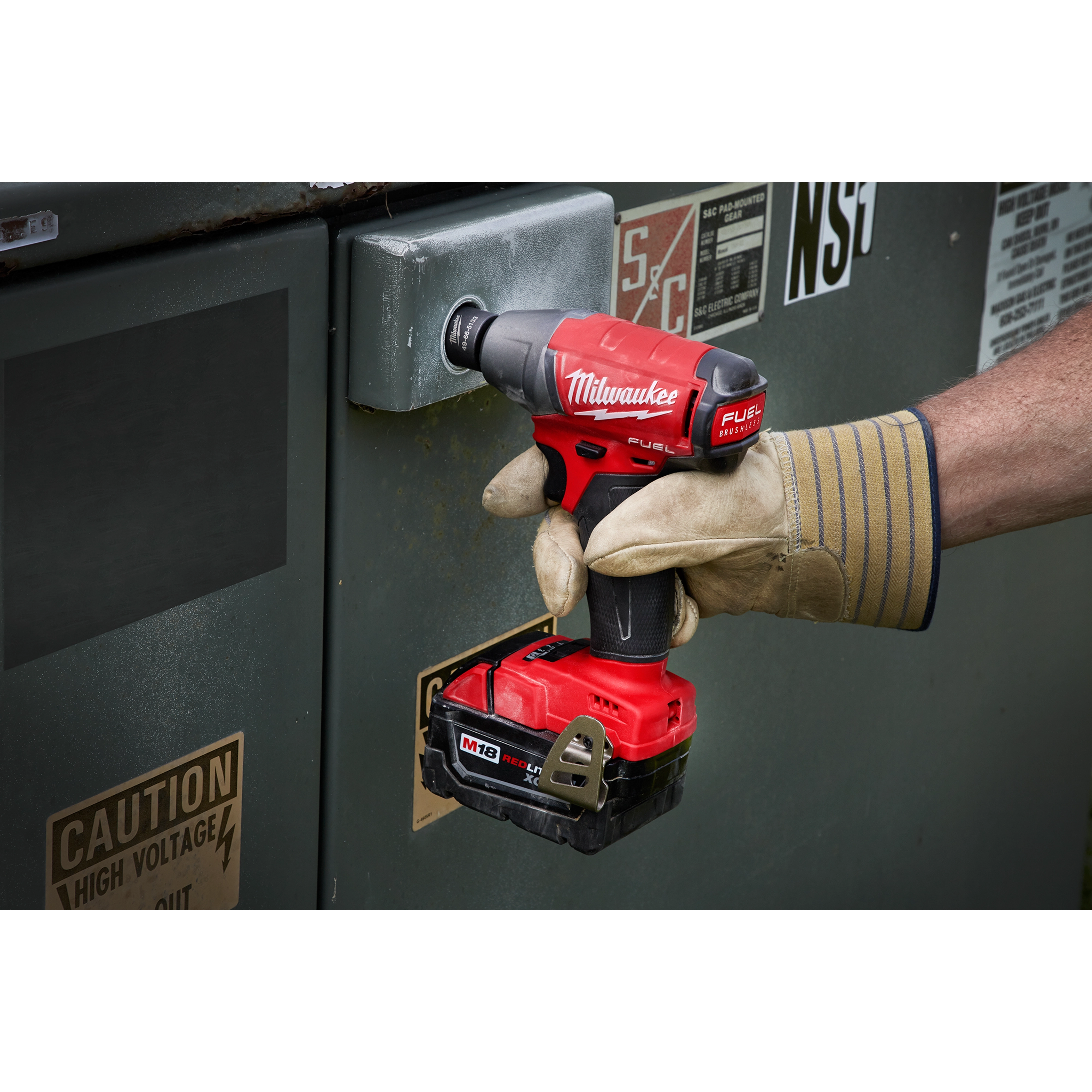 A gloved hand using the Penta%20Socket tool on a metal surface, marked with high voltage caution stickers.