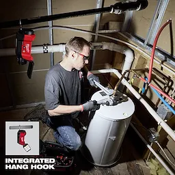 A worker uses a Milwaukee M12 FUEL Pipe Threader Kit to service a pipe system. The image showcases an integrated hang hook feature, allowing the tool to be suspended from a pipe. The equipment and accessories are neatly organized nearby.