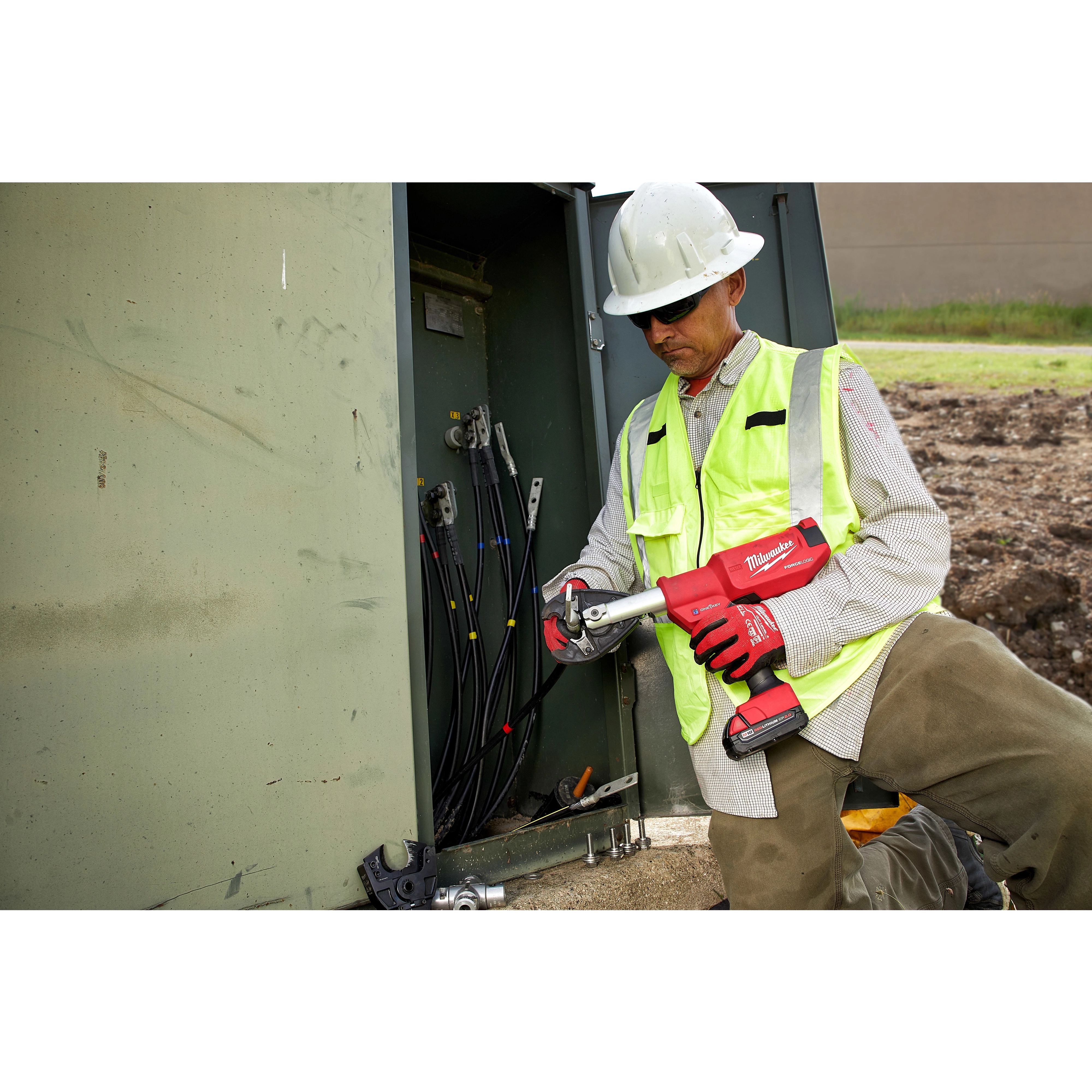 A utility worker uses the M18 FORCE LOGIC 6 Ton Pistol Utility Crimper to crimp wires in a large electrical box outdoors.