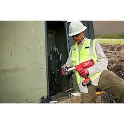 A utility worker uses the M18 FORCE LOGIC 6 Ton Pistol Utility Crimper to crimp wires in a large electrical box outdoors.
