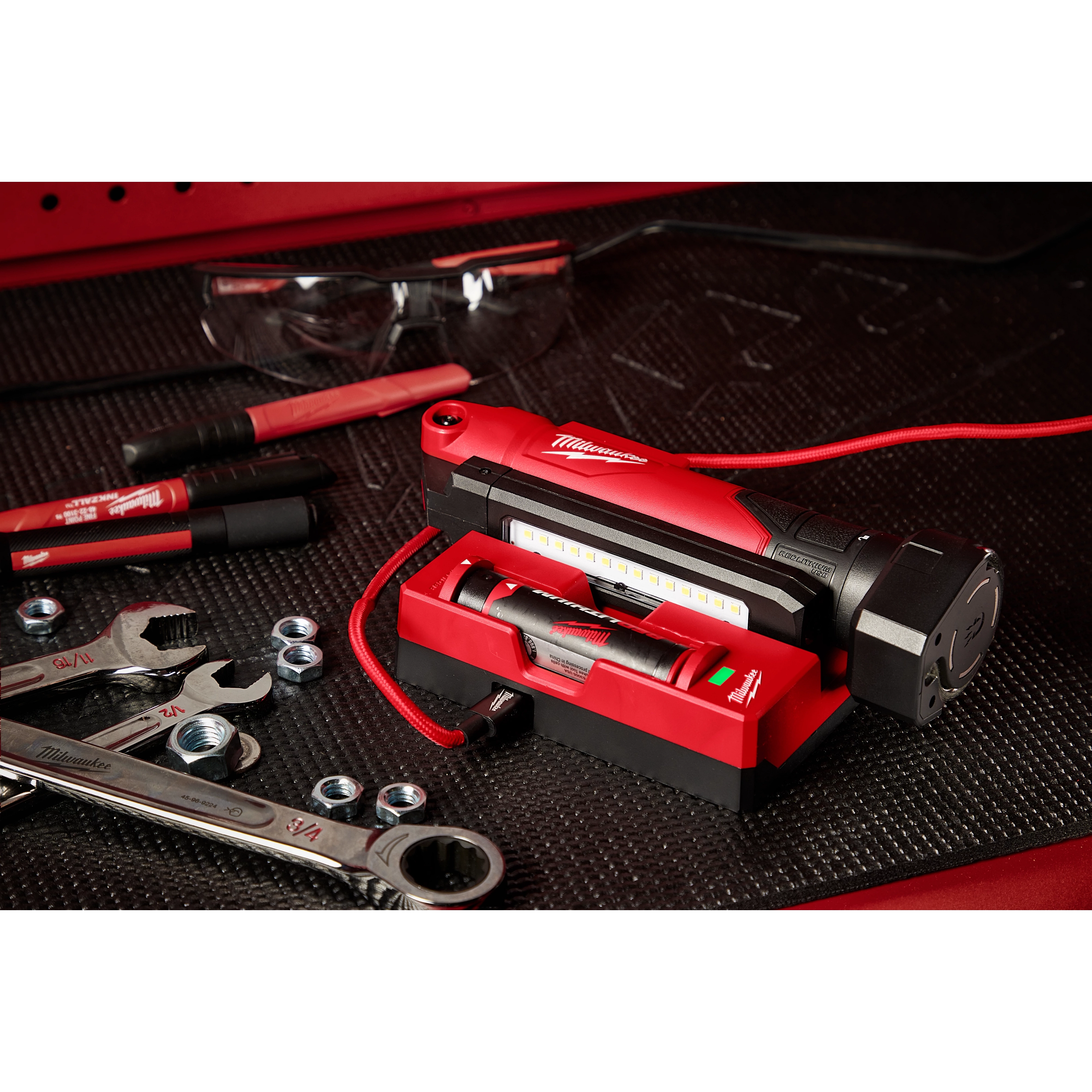 REDLITHIUM USB Stick Light w/ Magnet on a workbench with wrenches, nuts, markers, and safety glasses nearby.