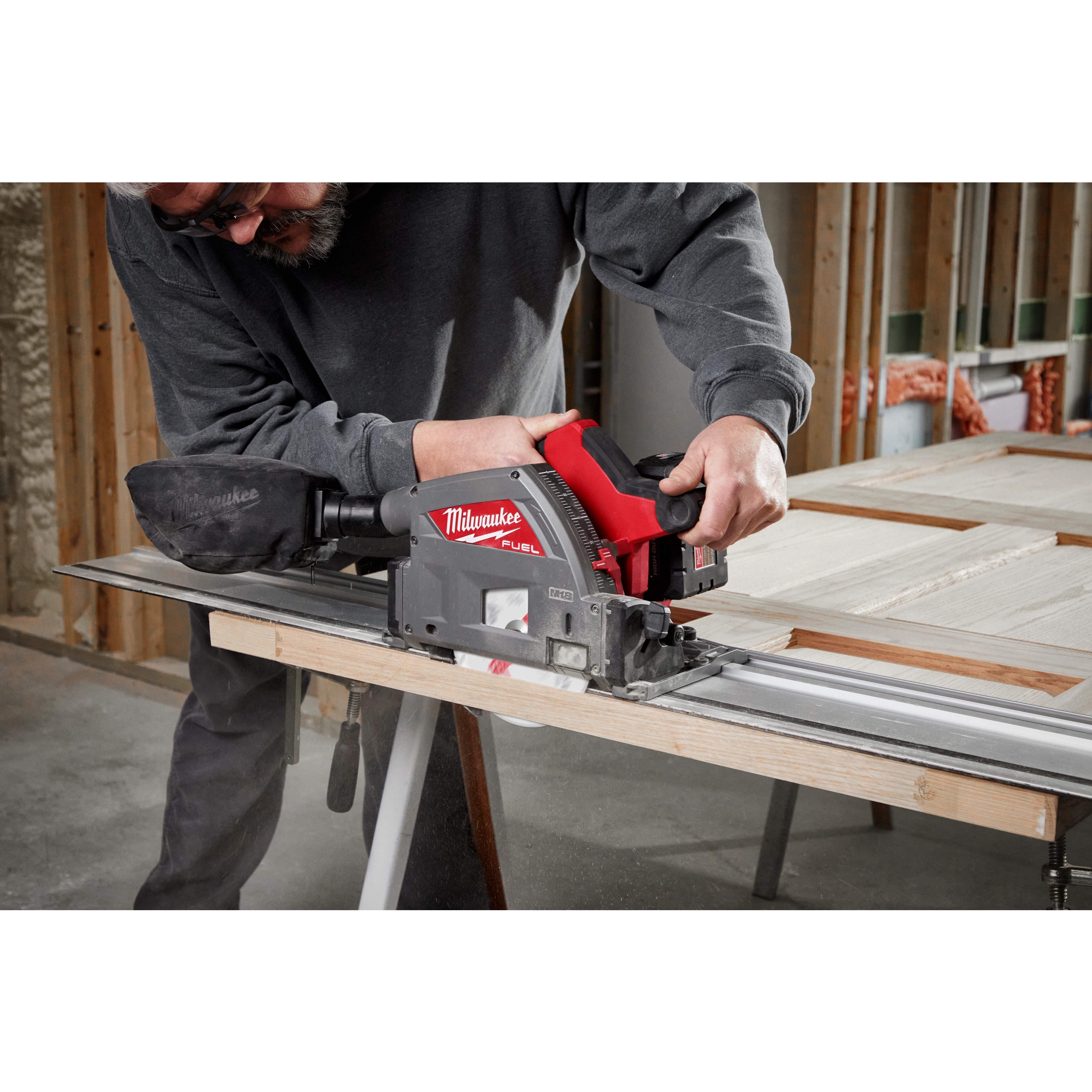 Person using the M18 FUEL 6 1/2" Plunge Track Saw to cut a piece of wood in a workshop.