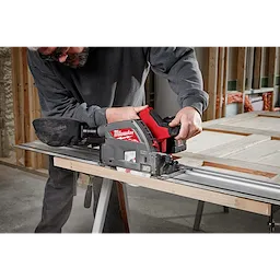 Person using the M18 FUEL 6 1/2" Plunge Track Saw to cut a piece of wood in a workshop.