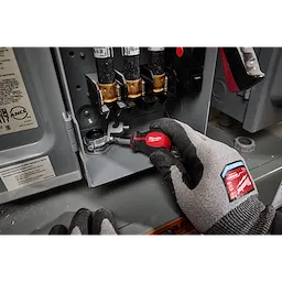 A person wearing gray gloves uses a 6-IN-1 Stubby Multi-Bit Screwdriver inside an electrical panel. The screwdriver has a red handle and multiple bit attachments.