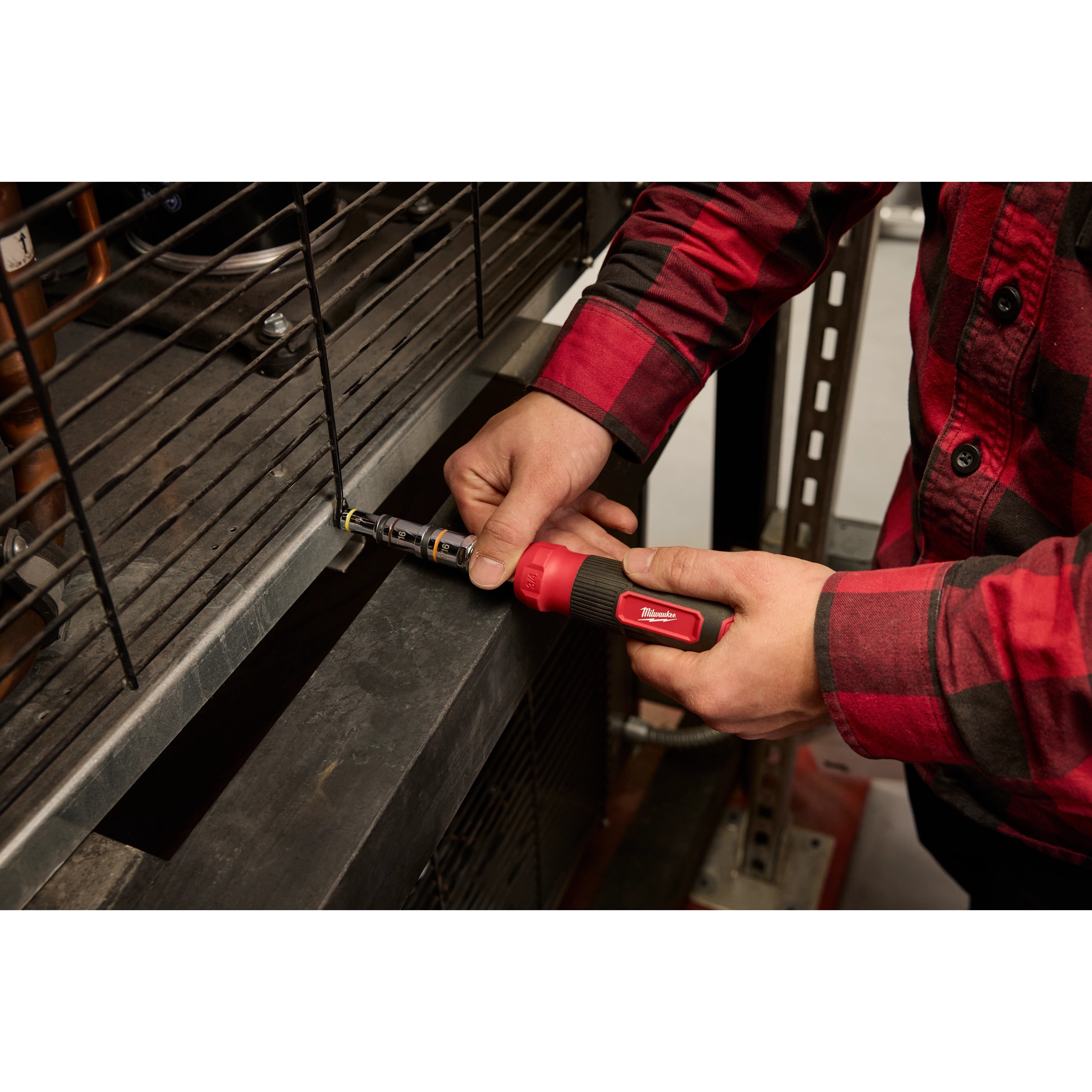 Person in a red plaid shirt using a 7-IN-1 HOLLOWCORE Multi-Nut Driver to tighten a bolt on a metal structure.