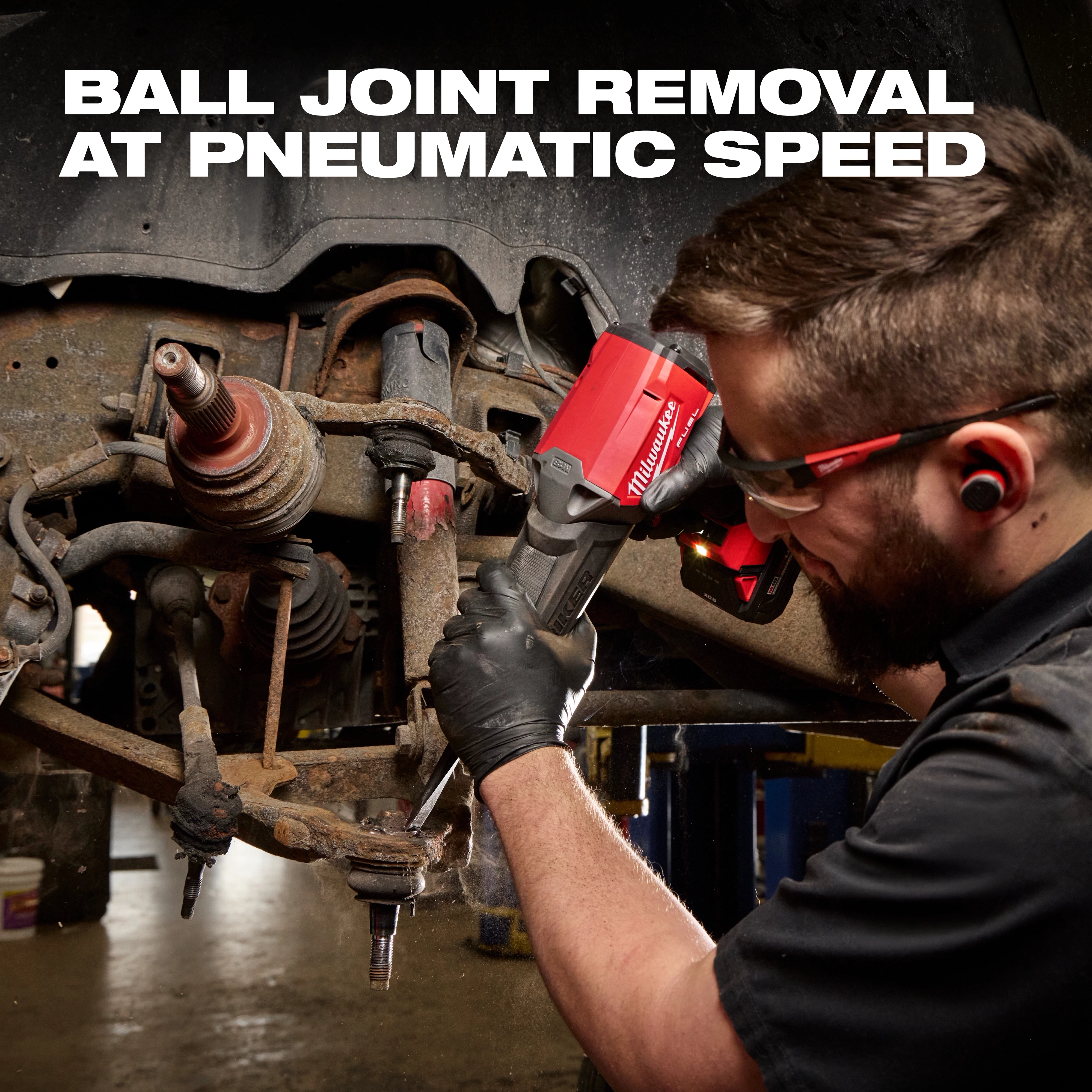 Mechanic using the red M18 FUEL STRIKER Hammer Chisel on a vehicle suspension assembly.