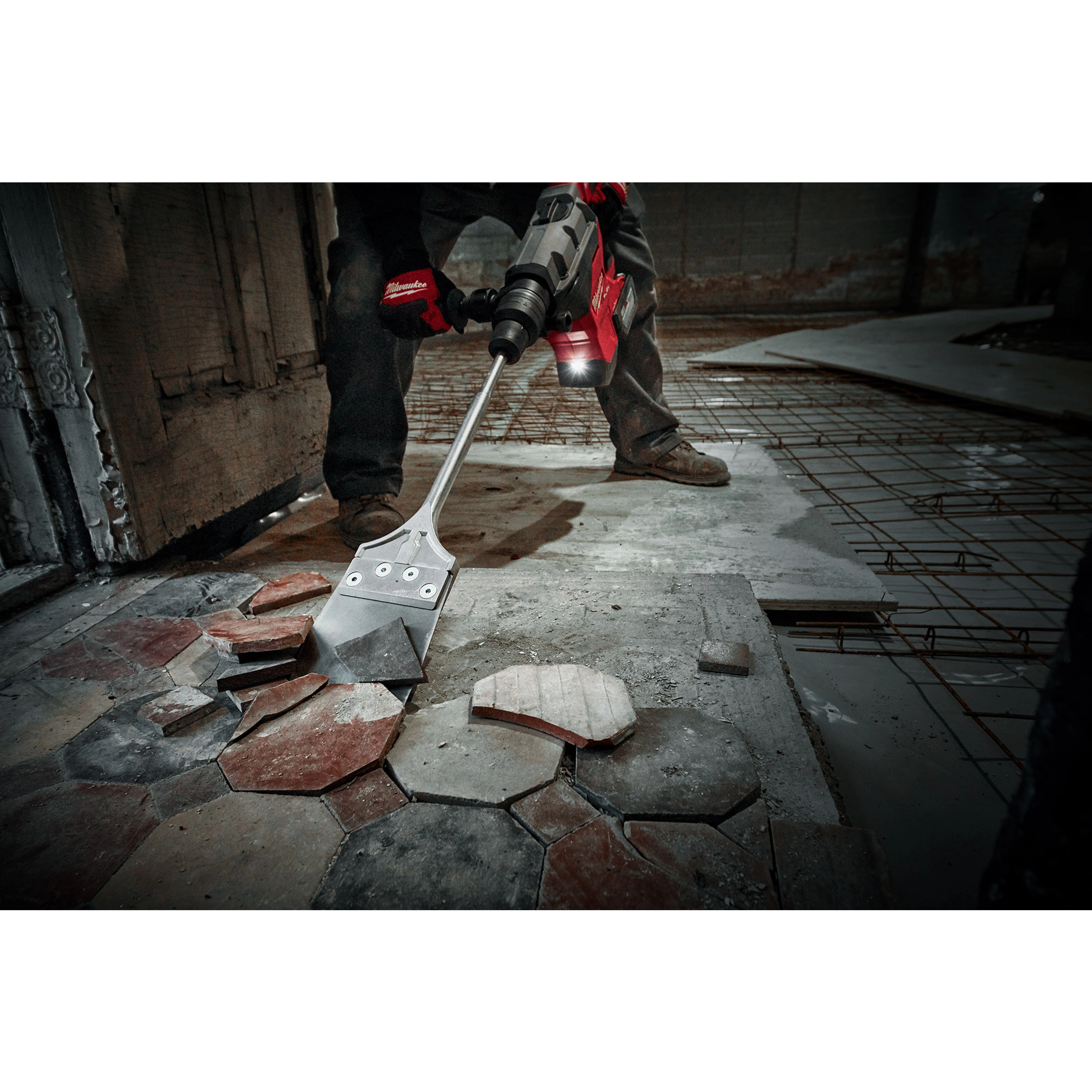 Worker using the SDS MAX Floor Scraper to remove old tiles from a concrete floor in a construction or renovation site.