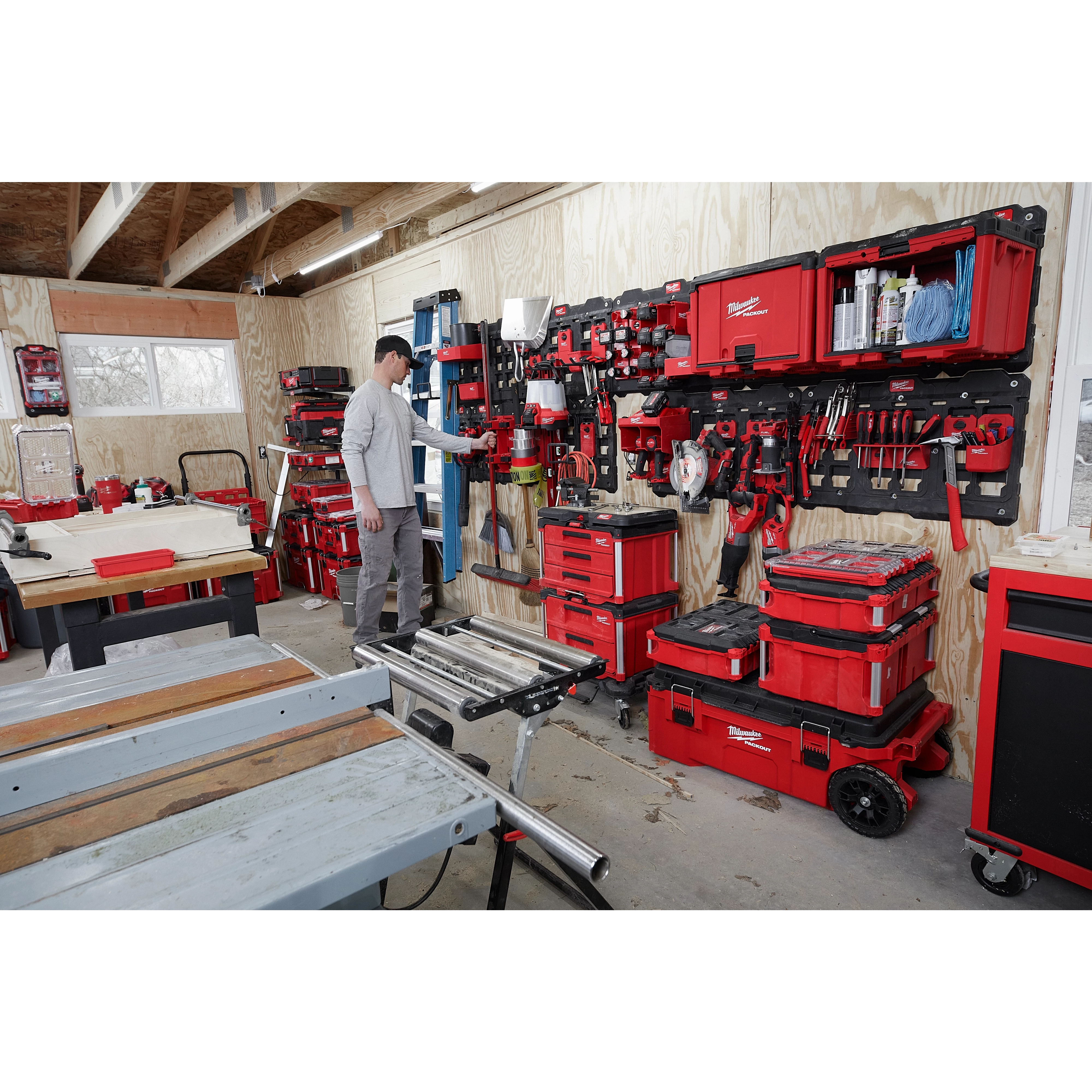 A man organizes tools on PACKOUT Large Wall Plate units in a workshop, surrounded by red storage boxes and woodworking equipment.