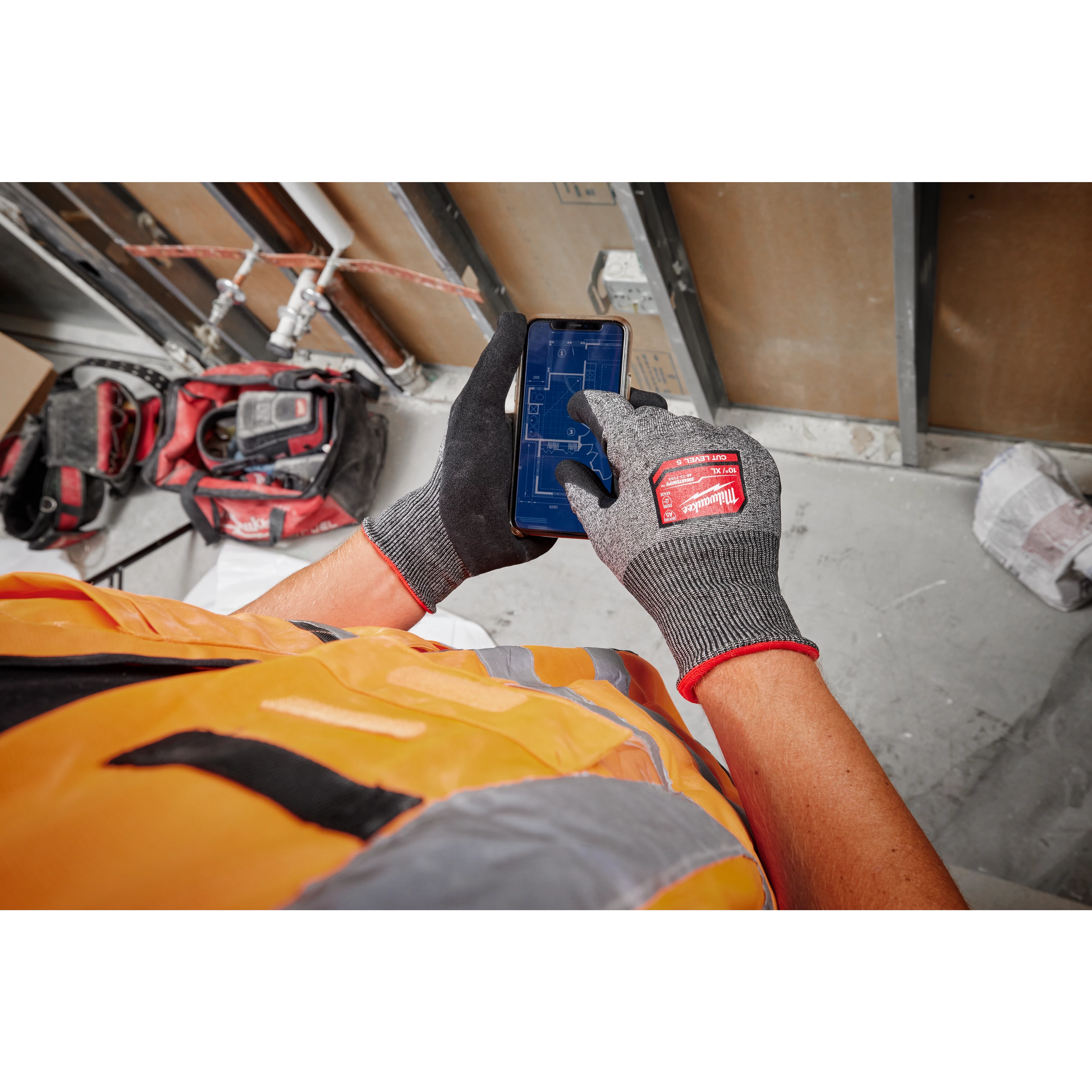 Cut Level 5 High-Dexterity Nitrile Dipped Gloves - L being worn by a person in a safety vest operating a smartphone in a work area.