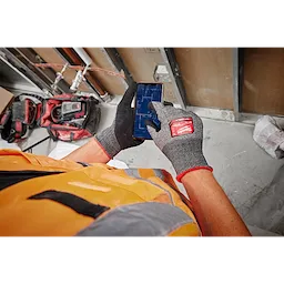Cut Level 5 High-Dexterity Nitrile Dipped Gloves - L being worn by a person in a safety vest operating a smartphone in a work area.