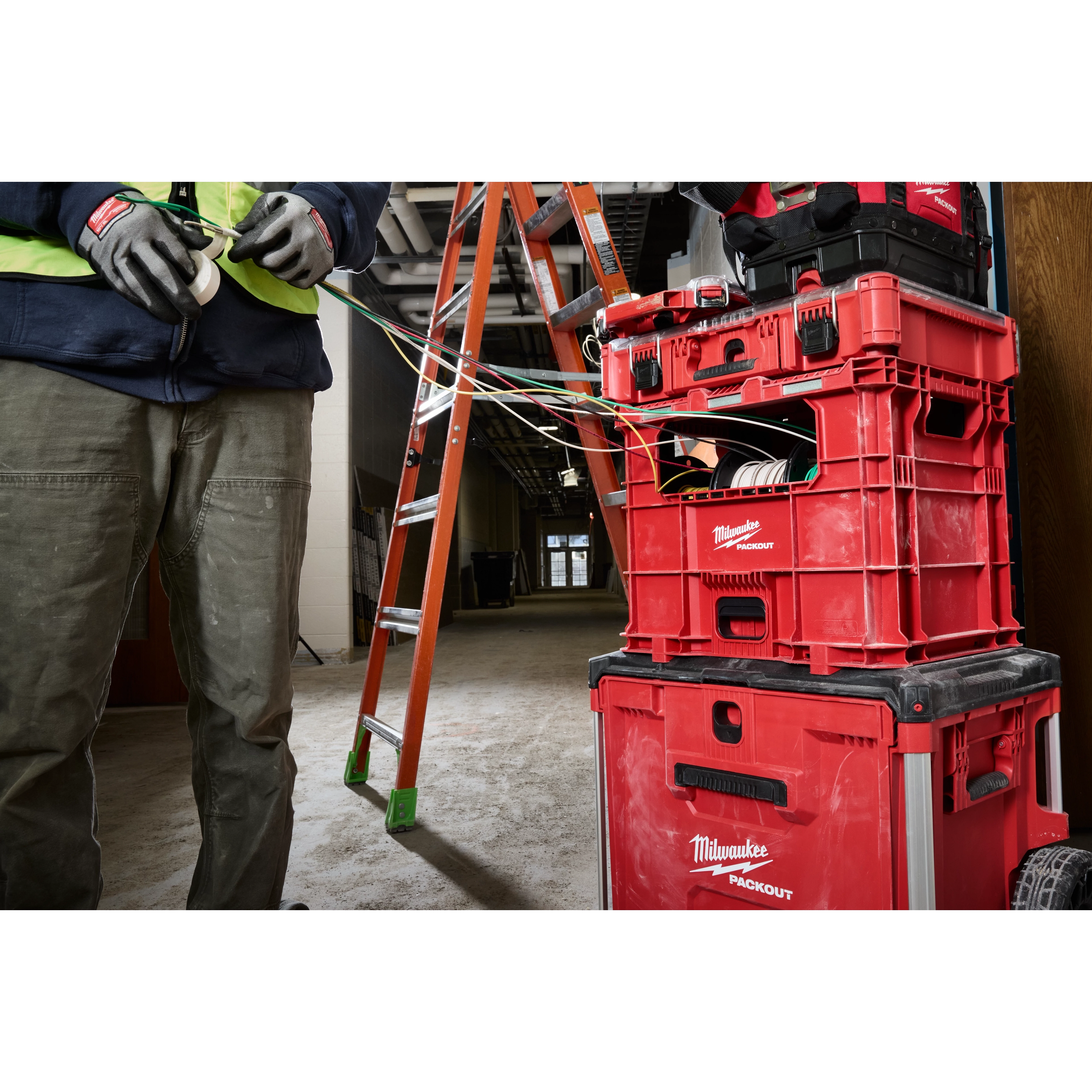 PACKOUT Wire Pulling XL Crate holding tools and wires in a construction setting with a worker and a ladder nearby.