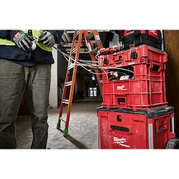 PACKOUT Wire Pulling XL Crate holding tools and wires in a construction setting with a worker and a ladder nearby.