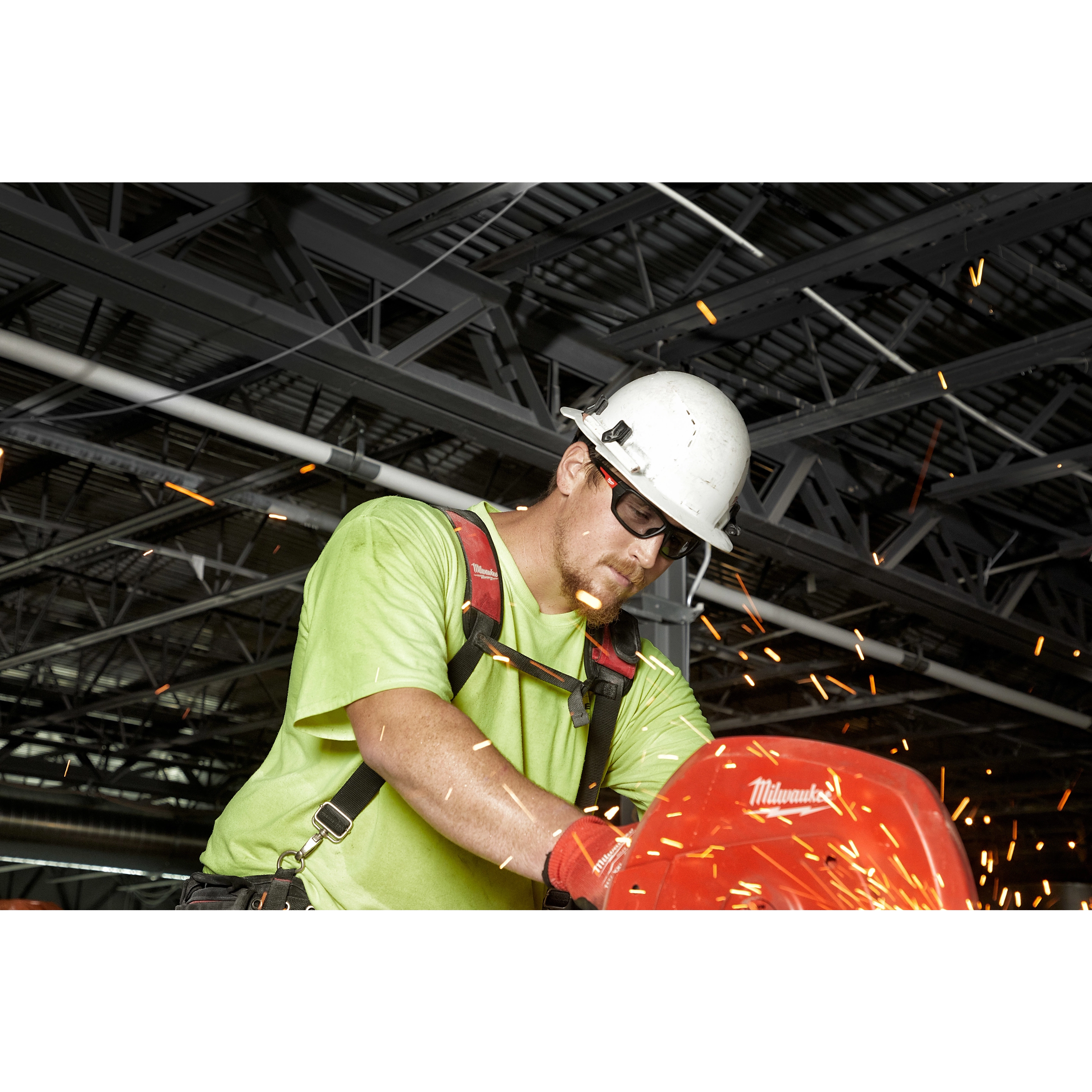 Worker in a green shirt using a power tool in a workshop with sparks flying and wearing Performance Safety Glasses - Gray Fog-Free Lenses.