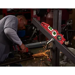 The Block Torpedo Level is clamped onto a metal frame in a workshop while a worker uses a power tool, creating sparks.