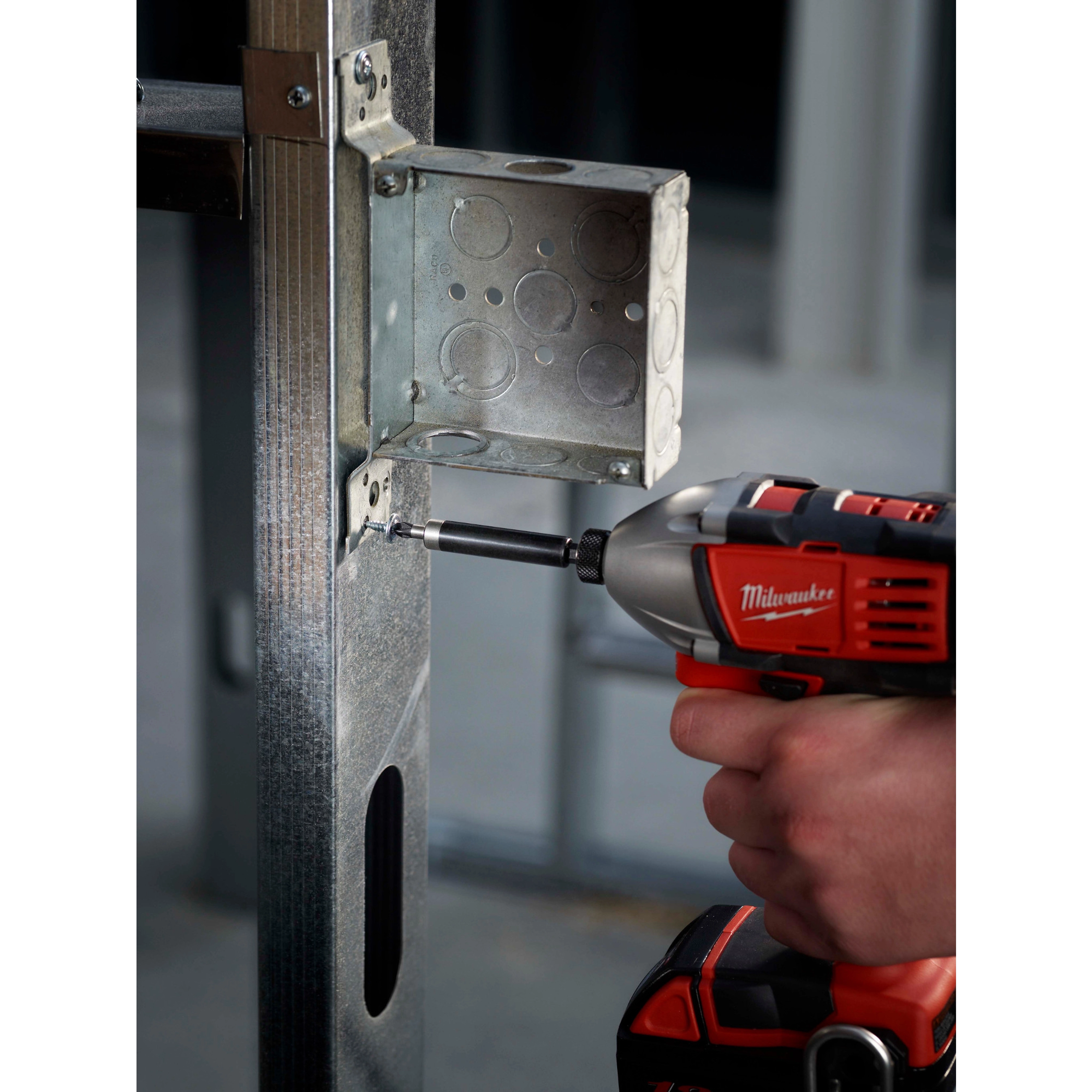 A person using a power drill with a Magnetic Bit Holder to install screws into a metal electrical box mounted on a frame.