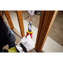 A person wearing gloves using 1000V Insulated 9" Lineman's Pliers to cut a red wire inside a wooden frame of a construction site.