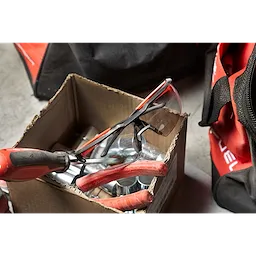 A pair of Safety Glasses - Gray Anti-Scratch Lenses is seen inside a cardboard box containing tools, including pliers.