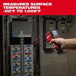 A person uses the Milwaukee infrared thermometer to measure temperatures on electrical panels, displaying a red laser dot for accurate targeting. The thermometer's screen shows readings, and text above indicates it measures surface temperatures from -22°F to 1,002°F.
